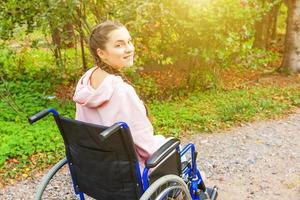 Young happy handicap woman in wheelchair on road in hospital park waiting for patient services. Paralyzed girl in invalid chair for disabled people outdoor in nature. Rehabilitation concept. photo