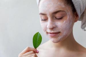 Woman face with green leaf and cream or nourishing mask photo