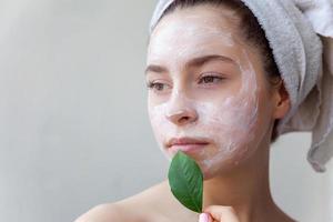 Woman face with green leaf and cream or nourishing mask photo