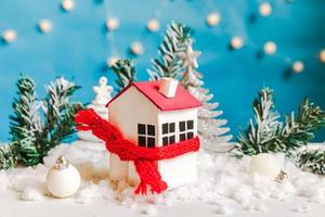 Abstract Advent Christmas Background. Toy house with knitted scarf with snow and winter decorations ornaments on blue background. Christmas with family at home concept. photo