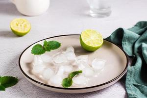 Melted ice cubes, lime and mint leaves on a plate on the table. Home made cocktails photo