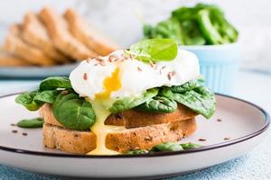 Appetizing sandwich with poached egg, spinach and flax seeds on a plate. Flexetarian Diet. Close-up photo