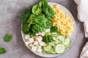 Bowl with pasta, cucumber, cheese and spinach on the table.  Top view. Close-up photo