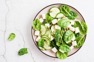 Fresh salad of cucumbers, spinach, cheese and pumpkin seeds in a plate. Top view. Close-up photo
