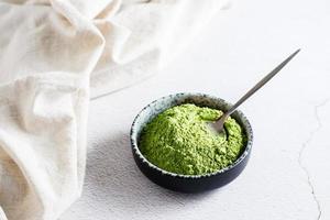 Organic green matcha tea powder in bowl and spoon on table photo
