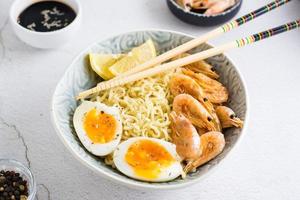 Chinese noodles with fried shrimp, boiled egg and lemon and chopsticks in a bowl on the table photo