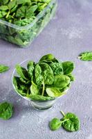 Fresh baby spinach leaves in a glass bowl and behind on a texture table. Vertical view. Close-up photo