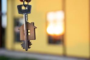 A hand with the keys to a new house on the background of an unfinished cottage. Building, project, moving to a new home, mortgage, rent and purchase real estate. To open the door. Copy space photo