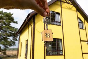 A hand with the keys to a new house on the background of an unfinished cottage. Building, project, moving to a new home, mortgage, rent and purchase real estate. To open the door. Copy space photo