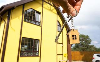 A hand with the keys to a new house on the background of an unfinished cottage. Building, project, moving to a new home, mortgage, rent and purchase real estate. To open the door. Copy space photo