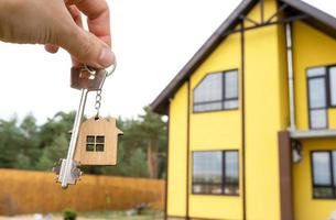 A hand with the keys to a new house on the background of an unfinished cottage. Building, project, moving to a new home, mortgage, rent and purchase real estate. To open the door. Copy space photo