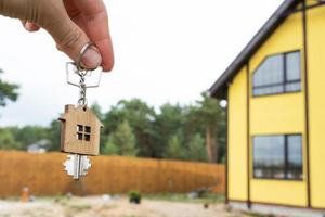 A hand with the keys to a new house on the background of an unfinished cottage. Building, project, moving to a new home, mortgage, rent and purchase real estate. To open the door. Copy space photo