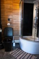 Loft-style toilet and shower, dark interior, combination of black and wood. Black toilet bowl, cozy knitted rug photo