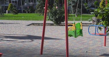 An empty children's swing swings in the wind at the playground video