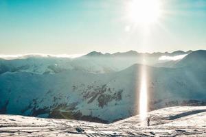 Caucasus mountains wide panorama in sunny day with snow crystals in air and skier stand enjoy holidays on piste. Gudauri Georgia travel winter destination photo