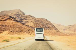 Back view white coach bus drive on asphalt road in scenic Wadi rum mountains in Jordan outdoors take tourist to destination. Cinematic tourism express bus copy space background photo