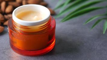 recipiente naranja de crema para la piel en la mesa con almendras enteras y fronda verde video