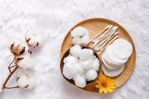 Organic cotton facial pads, cotton balls and cotton buds for removal makeup on wooden tray with natural cotton flowers on white fur background, hygiene and healthy care lifestyle photo