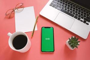 Flat lay of workspace desk and Apple iPhone XS with Grab application on the screen. Grab is an app for transportation and delivery service photo