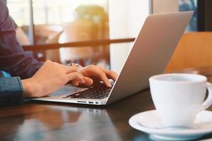 Close up of young businessman working remotely with computer laptop and coffee at home office during the spread of pandemic Covid-19 and Coronavirus, self quarantine and work from home photo