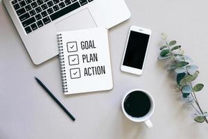 Goal, plan and action for 2020 on flat lay photo of workspace desk with smartphone, coffee, laptop and notebook with copy space background, minimal style and mockup concept