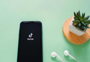 Flat lay of iPhone XS showing Tik Tok application on screen with earphones and plant, Tik tok is popular social media network and entertainment photo