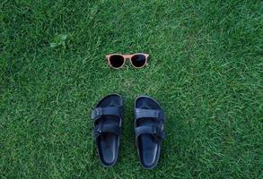 Flat lay summer fashion accessories concept of sunglasses and sandals shoes on green grass background, vacation and summertime background photo