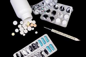 Medical pills flow from a white jar on an isolated black background with reflection a thermometer photo