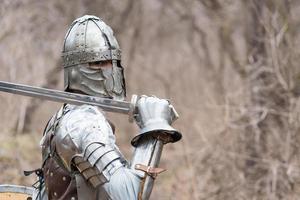 noble guerrero. retrato de un guerrero medieval o caballero con armadura y casco con escudo y espada posando foto