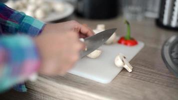 dichtbij omhoog van een vrouw handen snijdend champignons Aan de keuken bord. video