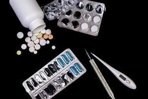 Medical pills flow from a white jar on an isolated black background with reflection a thermometer photo