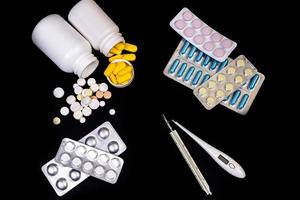 Medical pills flow from a white jar on an isolated black background with reflection a thermometer photo