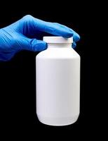 Medical pills in white jar on an isolated black background with reflection in hand photo