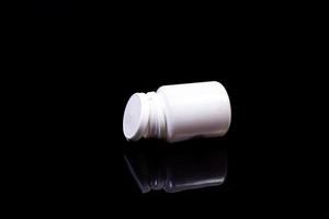 Medical pills in white jar on an isolated black background with reflection photo