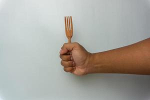 Mano sujetando cuchara y tenedor de madera aislado sobre fondo blanco. foto