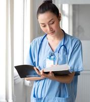 mujer médico persona usa uniforme y estetoscopio leyendo documento de información del paciente para consulta de cirugía. enfermera profesional asiática está trabajando como consulta de atención médica en el hospital foto