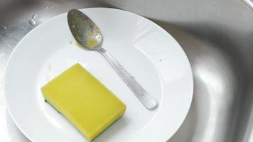 Dirty dish and spoon in sink with yellow sponge video