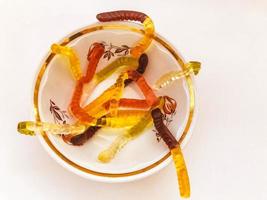 gusanos gomosos yacen en un plato de porcelana blanca. postre dulce alto en calorías en un plato hondo. gominolas gelatinosas brillantes de diferentes colores foto