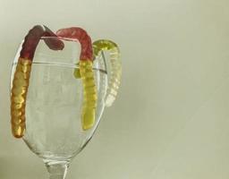 gummy worms in a transparent glass with water. bright, sweet gummy worms drown in water. still life on a white matte background. sweet high-calorie dessert photo