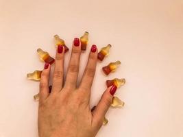 marmalade candies. sweets in the form of a bottle with lemonade. the chewing gum is in the shape of a circle. rays of the sun from sweets on a yellow matte background, top hand with red manicure photo