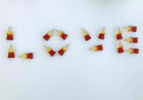 the word love is laid out on a white matte marmalade background. gelatin candy in the form of bottles with lemonade. sweet appetizing dessert. creative lettering photo