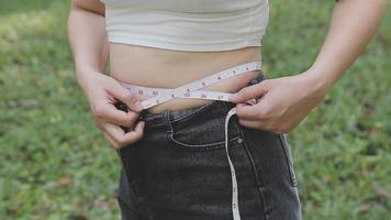 hermosa mujer gorda con cinta métrica usa su mano para exprimir el exceso de grasa que está aislado en un fondo blanco. ella quiere perder peso, el concepto de cirugía y descomponer grasa bajo el video