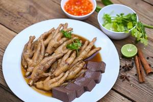 comida tailandesa, sopa de patas de pollo guisada, cocinando estofado de patas de pollo en blanco con ingredientes de hierbas y especias con vegetales de limón picante sobre fondo de madera, estofado de menú de comida china asiática foto