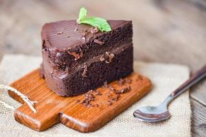 pastel de chocolate delicioso postre servido en la mesa - rebanada de pastel sobre fondo de tablero de corte de madera con chocolate y hoja de menta foto