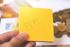 Debt concept with write debt on paper in hand and coins on table background photo