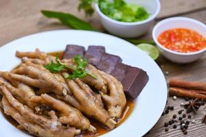 comida tailandesa, sopa de patas de pollo guisada, cocinando estofado de patas de pollo en blanco con ingredientes de hierbas y especias con vegetales de limón picante sobre fondo de madera, estofado de menú de comida china asiática foto