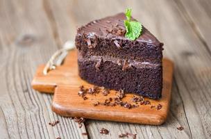 Cake chocolate delicious dessert served on the table - cake slice on wooden cutting board background with chocolate and mint leaf photo