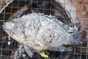 Pescado a la parrilla - cerca de pescado tilapia a la parrilla con sal al fuego y humo, pescado quema comida asiática foto