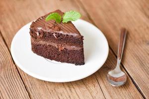 Cake chocolate delicious dessert served on the wooden table - cake slice on white plate with topping chocolate and mint leaf photo