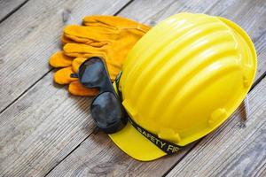 equipo de seguridad seguridad de construcción estándar ropa de trabajo de protección industrial herramienta con sombrero amarillo casco de seguridad gafas y guantes sobre fondo de madera foto